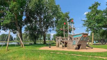 A playground with a pirate-themed play structure, including a ship and climbing elements, surrounded by trees and grassy areas.