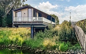 Una cabaña moderna y elevada con balcón, ubicada sobre una masa de agua, rodeada de exuberante vegetación.