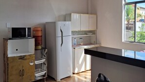 Une cuisine compacte équipée d’un réfrigérateur, d’un four à micro-ondes et d’un distributeur d’eau. Une fenêtre offre une lumière naturelle et une vue sur l’extérieur.