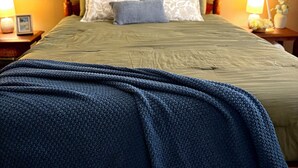 Ein Himmelbett mit grüner Bettdecke, weißen Kissen mit Muster und einer blauen Strickdecke.
