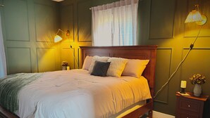 Ein ordentlich bezogenes Bett mit Holz-Kopfteil, ein Nachttisch mit Lampe und eine Vase mit Blumen.