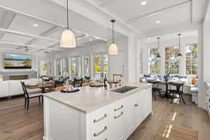 A spacious kitchen with a large island, pendant lighting, and a view of the outdoors through large windows. - Kingfish House: Luxury Canal Home, Boat Dock, Pool, Spa by Anna Maria Life Vacation Rentals (Anna Maria)
