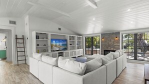Ein geräumiges Wohnzimmer mit einem großen, weißen Modulsofa, einem Flachbildfernseher, integrierten Regalen und einem Kamin aus Naturstein.