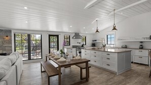 Eine moderne Küche mit weißen Schränken, einer großen Kochinsel und einem Essbereich mit Holztisch und Bank.