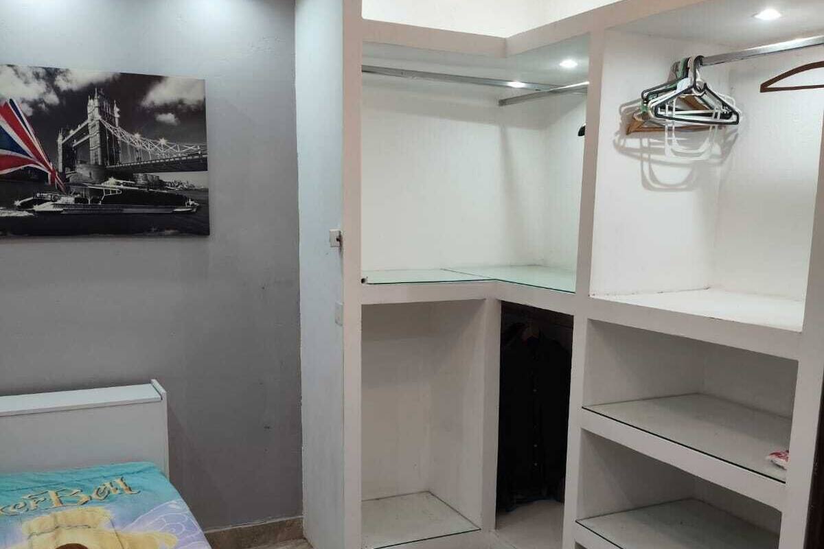 A bedroom with a bed, a ceiling fan, a wardrobe, and a shelf unit.
