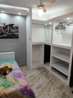 Un dormitorio con una cama, ventilador de techo, armario y estantería.