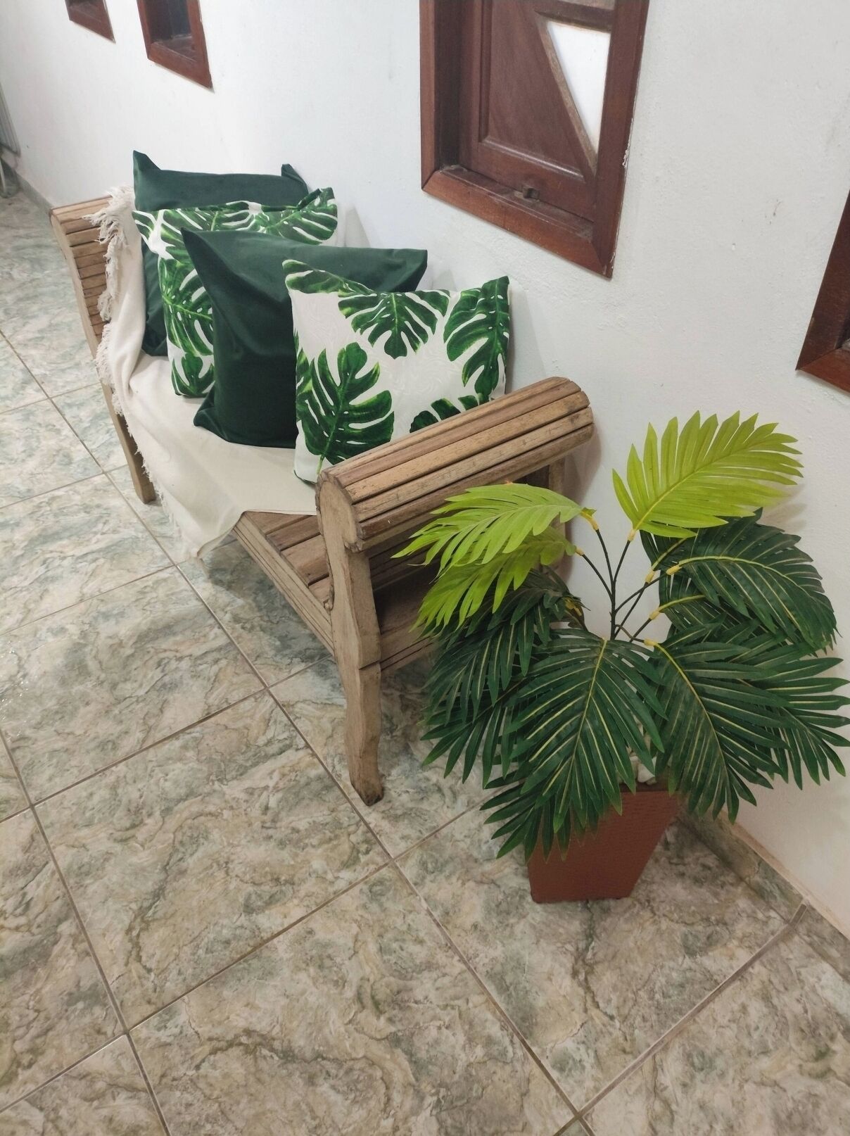 Un banco de madera con cojín, una planta en maceta y una pared con ventana.