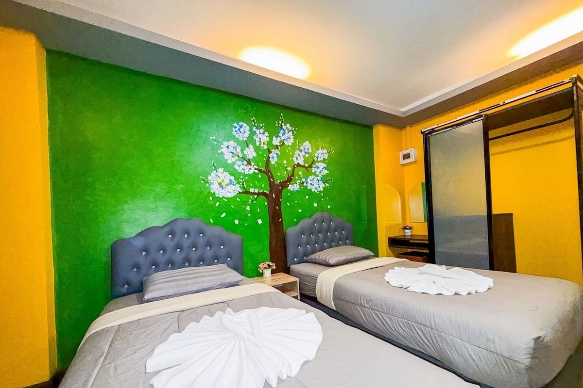 A hotel room with two beds, a green wall with a tree mural, and a sliding door.