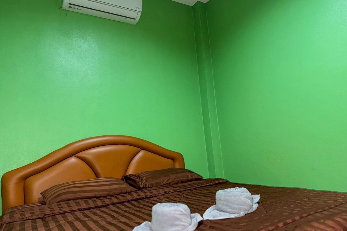 A hotel room with a bed, pillows, and a green wall.