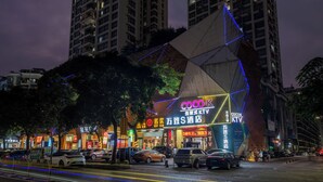 Un edificio moderno con una fachada geométrica distintiva, señalización iluminada y un estacionamiento con automóviles.