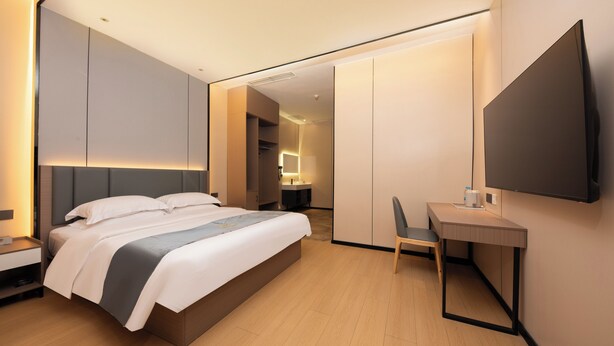 Habitación de hotel moderna con cama, escritorio, silla y televisor montado en la pared.