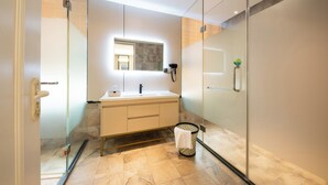 Un baño moderno con cabina de ducha de vidrio, tocador blanco con espejo y suelo de baldosas de piedra.