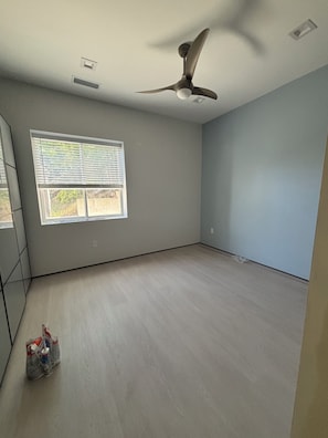 Una habitación con ventilador de techo, una ventana con persianas y suelo de madera claro.
