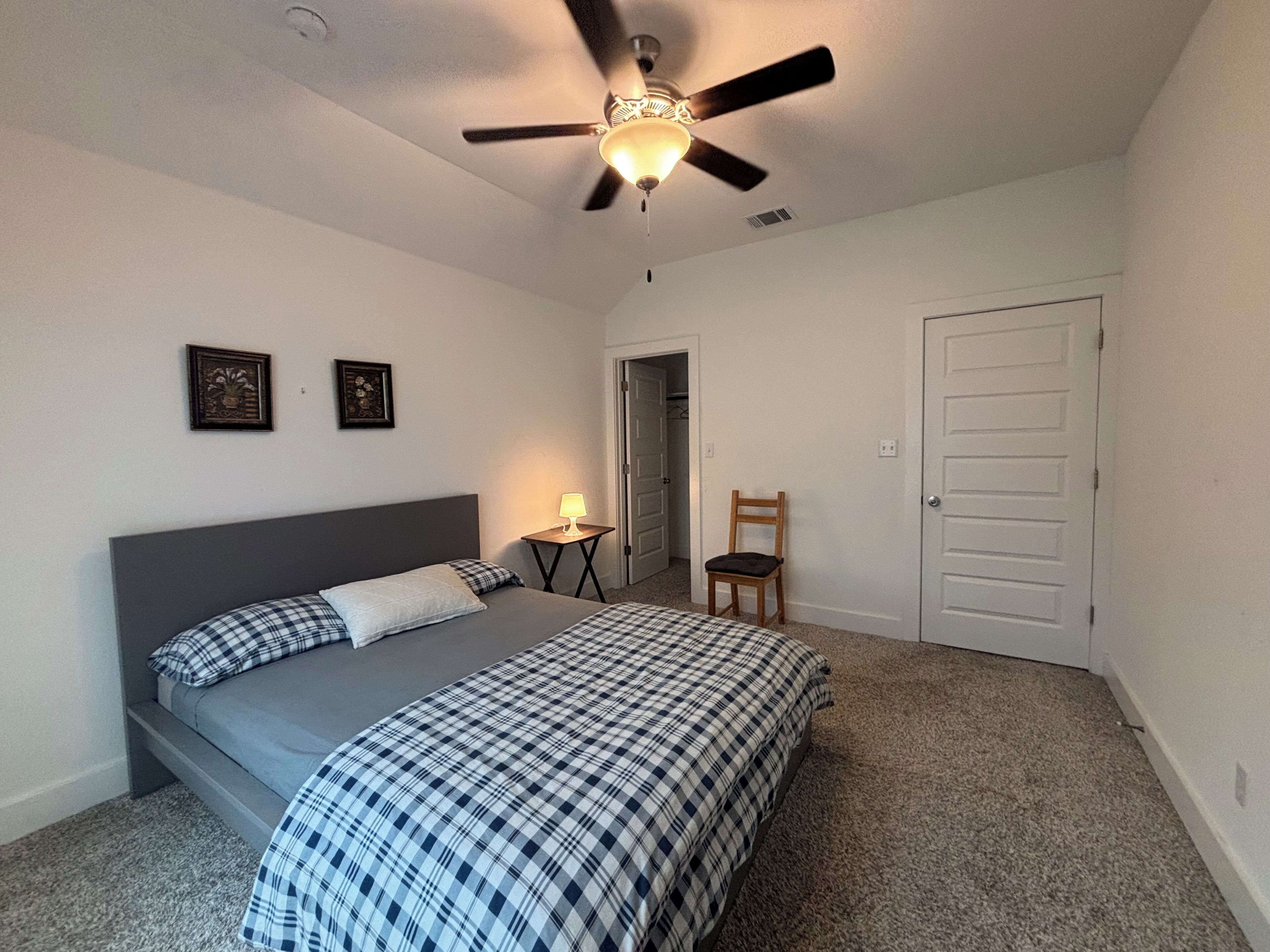 A bedroom with a bed, a ceiling fan, a nightstand, a chair, and a door.