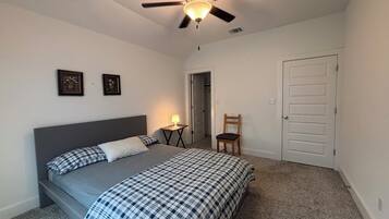 A bedroom with a bed, a ceiling fan, a nightstand, a chair, and a door.