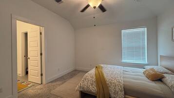 A bedroom with a bed, a ceiling fan, a window with blinds, and a door leading to another room.