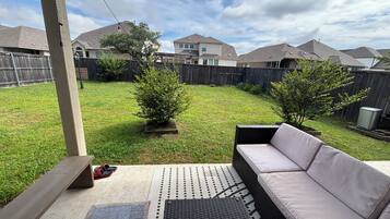 A backyard patio with a cushioned outdoor seating area, a small tree, and a wooden fence.