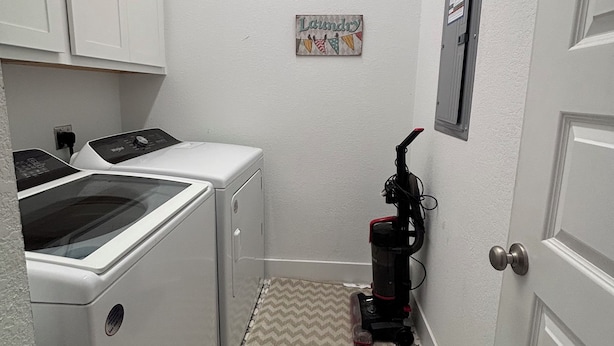 A laundry room with a washing machine, a dryer, a vacuum cleaner, and a door with a sign above it.