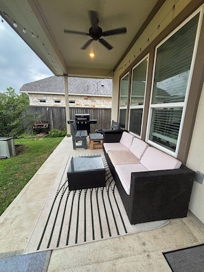An outdoor patio with a ceiling fan, a grill, and a sofa.