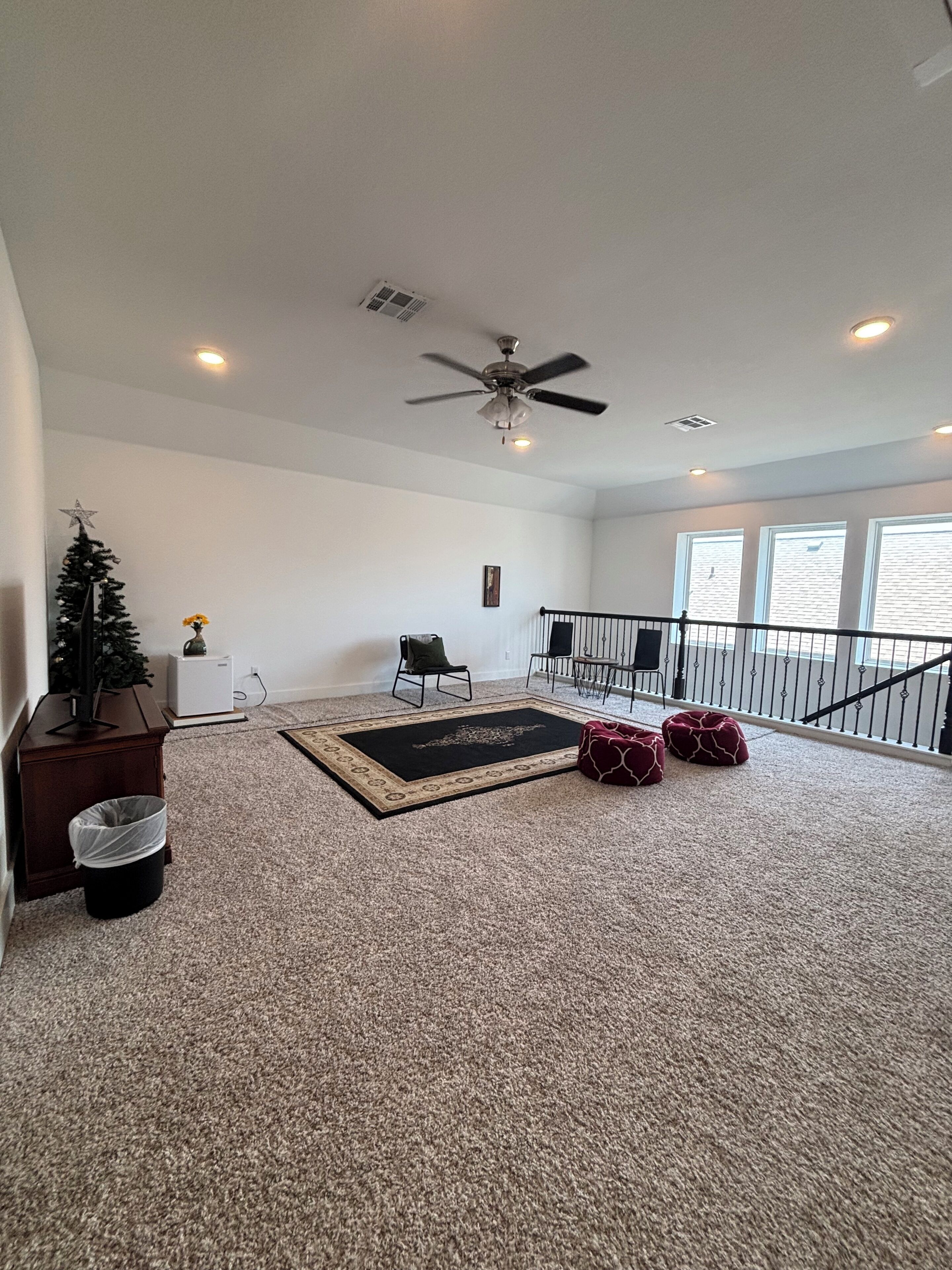 A spacious living area with a ceiling fan, a small Christmas tree, and a view of the outside through large windows.