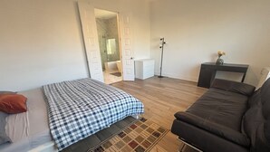 A bedroom with a bed, a sofa, a small desk, and a bathroom visible through an open door.