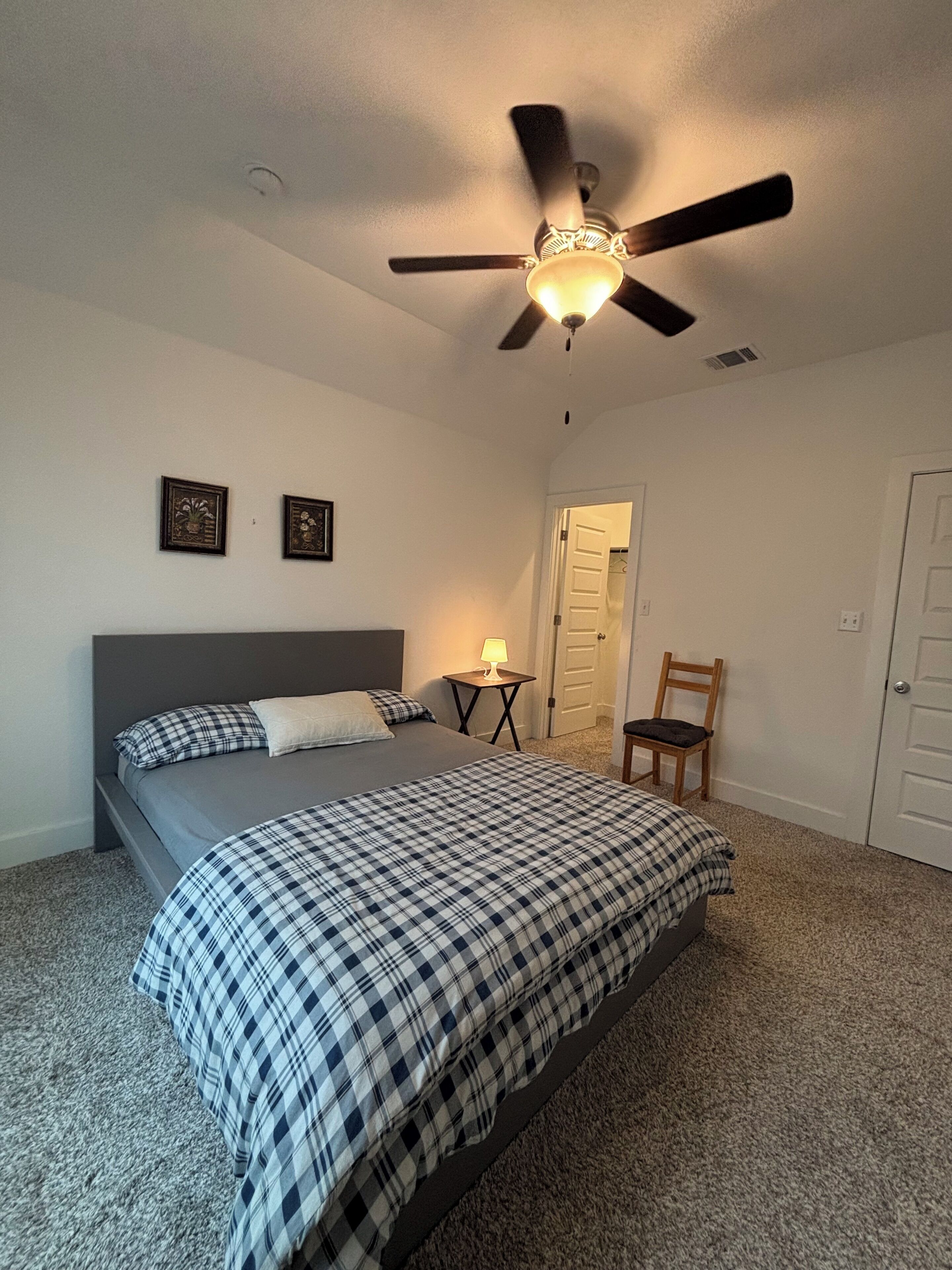 Ein Schlafzimmer mit Bett, Deckenventilator, Nachttisch, Stuhl und Tür.