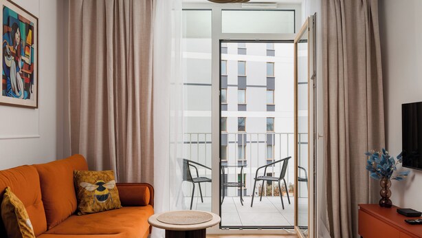 Ein modernes Wohnzimmer mit einer Couch, einem kleinen runden Tisch und einem Balkon mit Sitzgelegenheiten.