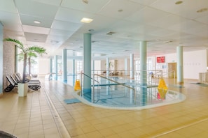 A spacious indoor swimming pool area with clear water, surrounded by tiled floors and columns, and equipped with safety railings. - Diva SPA Seaside Studio (Kołobrzeg)