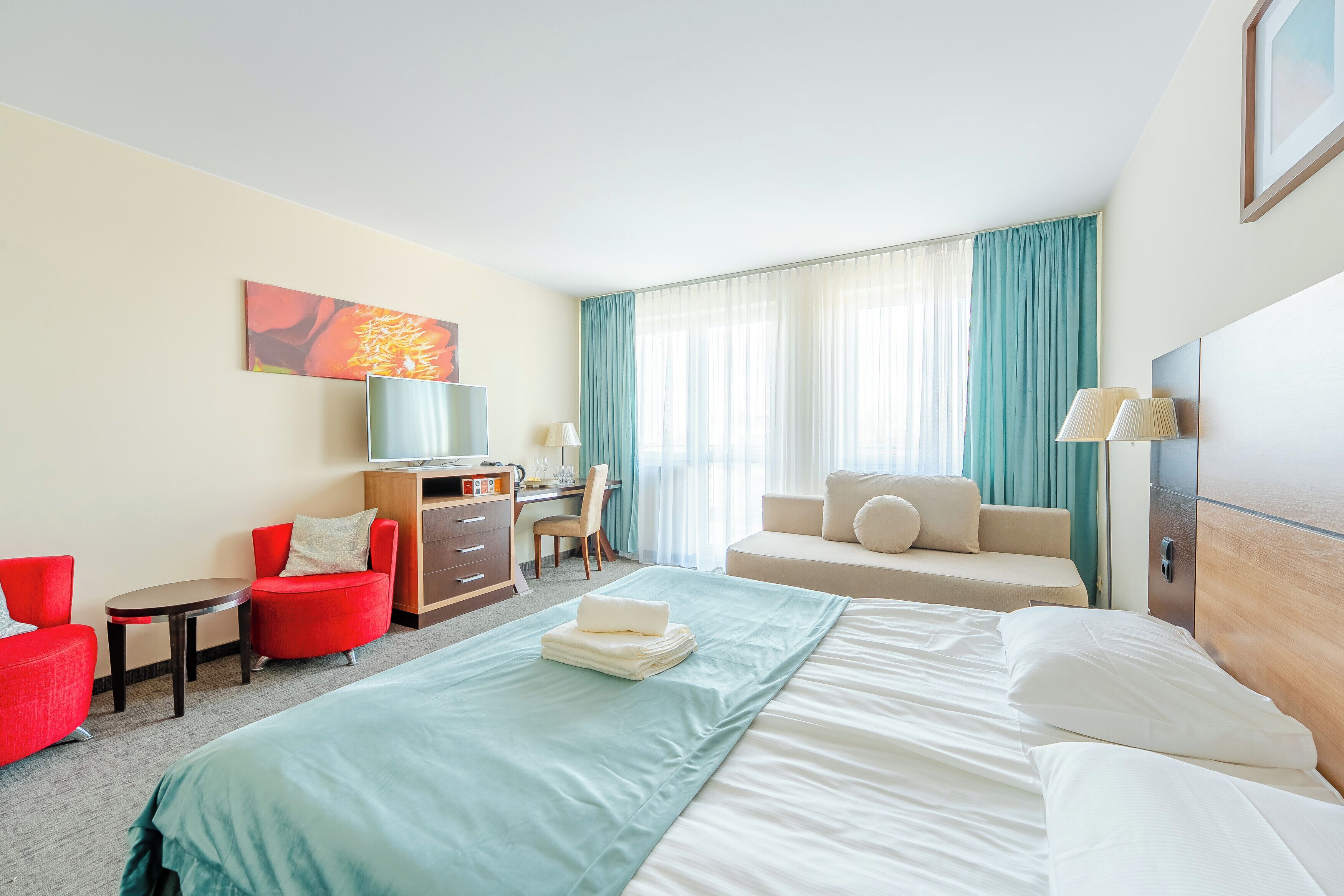 A hotel room with a bed, a desk, a chair, and a sofa.