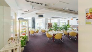 Un amplio comedor con mesas redondas y sillas amarillas, ventanas grandes e iluminación de techo.