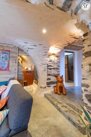 Ein gemütliches Interieur mit einer Steinwand, einer Couch, einer Bärenskulptur und einer durch einen Bogen sichtbaren Küche.