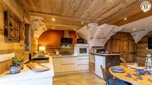 A rustic kitchen with wooden beams, a central island, and a dining area with a round table. - LE GITE DE LA MONTAGNETTE (BEAUNE)