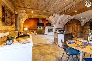 Eine rustikale Küche mit Holzbalken, einer zentralen Kochinsel und einem Essbereich mit einem runden Tisch.