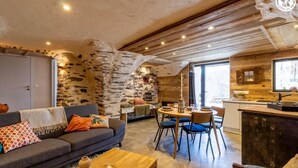 A cozy living room with a stone wall, a sofa, a coffee table, and a dining area with chairs and a table. - LE GITE DE LA MONTAGNETTE (BEAUNE)