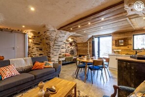 Ein gemütliches Wohnzimmer mit Steinwand, einer Couch, einem Couchtisch und einem Essbereich mit Stühlen und Tisch.