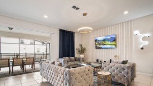 Un salon moderne avec un canapé d’angle, un coin repas comprenant une table et des chaises, et une grande fenêtre agrémentée de rideaux.