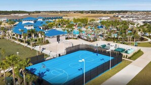 Vue aérienne d’un quartier résidentiel avec un grand terrain de basket-ball bleu, entouré de maisons et de palmiers.