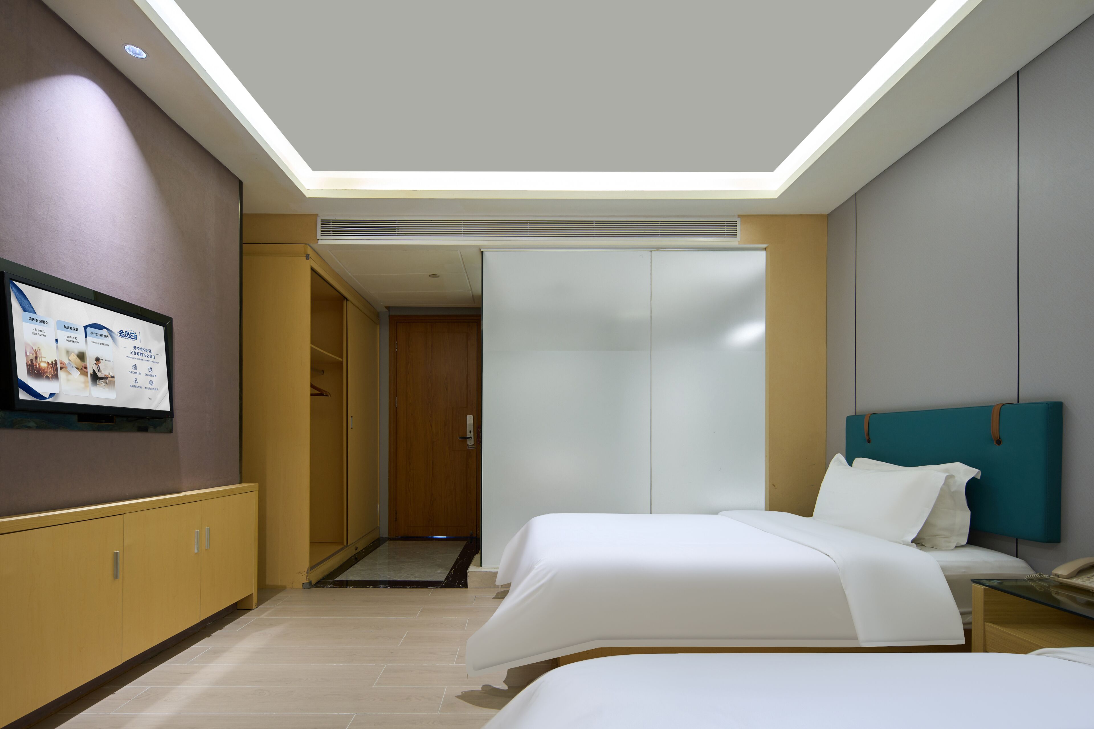 A hotel room with two beds, a TV mounted on the wall, a wardrobe, and a ceiling light.