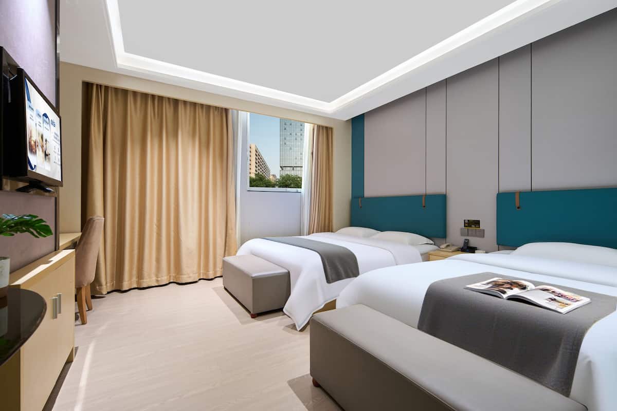 Een moderne hotelkamer met twee bedden, een bureau, een televisie en een raam met gordijnen.