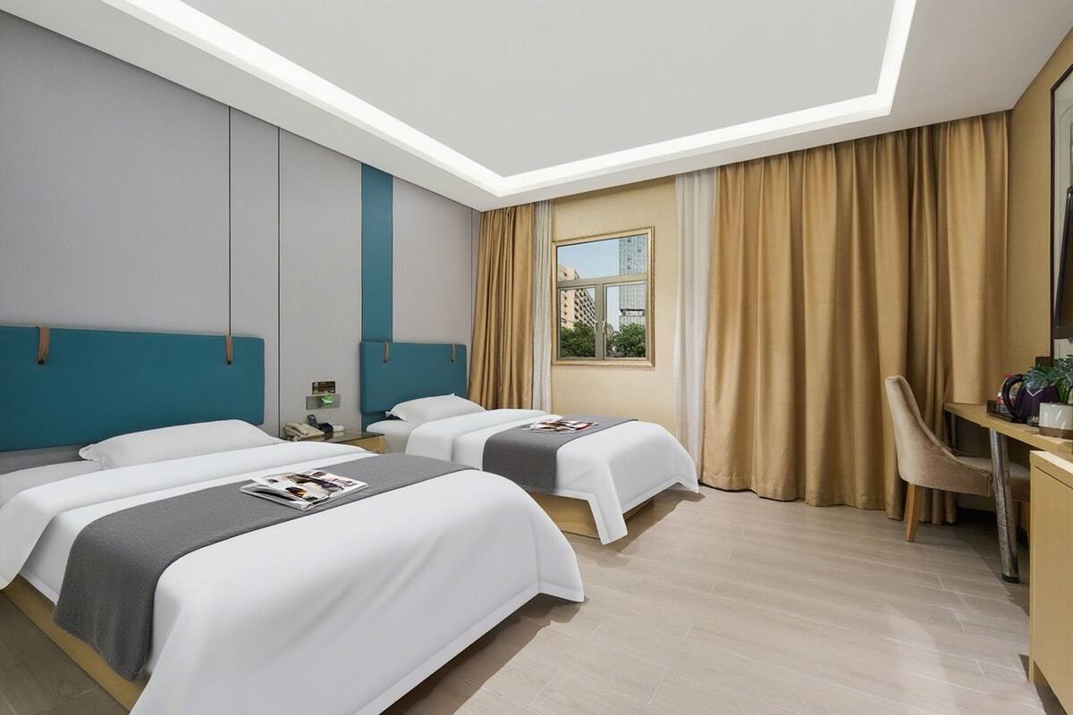 Een hotelkamer met twee bedden, een bureau en een raam met gordijnen.