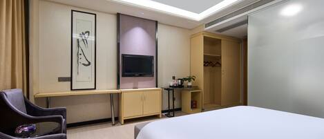 Habitación de hotel con cama, escritorio, televisor, armario y una silla.