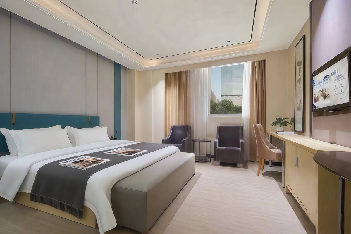 Een moderne hotelkamer met een groot bed, een bureau, twee stoelen, een bijzettafeltje en een televisie aan de muur.