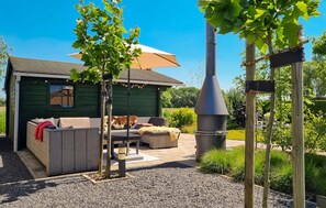 Een terras met buitenmeubilair, een barbecue en een groen gebouw op de achtergrond.