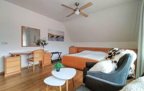 Un dormitorio con cama, escritorio, silla, mesita y ventilador de techo, además de una ventana.