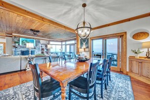 A spacious dining area with a wooden table and chairs, a chandelier, and a view of the ocean through large windows. - 3BR Home w/180° Mountain Views | Hot Tub, Poker Room, Sauna | 5 Min to Ski Resort (Beech Mountain)