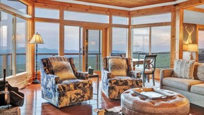 A spacious room with large windows, wooden ceiling, and a mix of seating including chairs and a sofa. - 3BR Home w/180° Mountain Views | Hot Tub, Poker Room, Sauna | 5 Min to Ski Resort (Beech Mountain)
