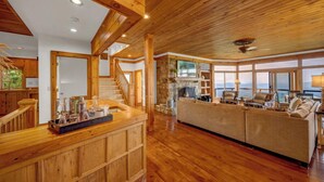 A spacious living area with a wooden ceiling, a stone fireplace, and a large window overlooking a scenic view. - 3BR Home w/180° Mountain Views | Hot Tub, Poker Room, Sauna | 5 Min to Ski Resort (Beech Mountain)