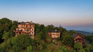 A large, multi-story house with a balcony on the upper floor, surrounded by dense forest and hills in the background. - 3BR Home w/180° Mountain Views | Hot Tub, Poker Room, Sauna | 5 Min to Ski Resort (Beech Mountain)