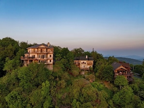 A large, multi-story house with a balcony on the upper floor, surrounded by dense forest and hills in the background. - 3BR Home w/180° Mountain Views | Hot Tub, Poker Room, Sauna | 5 Min to Ski Resort (Beech Mountain)