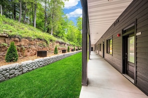 A building with a covered walkway, stone retaining wall, and a grassy area with trees.